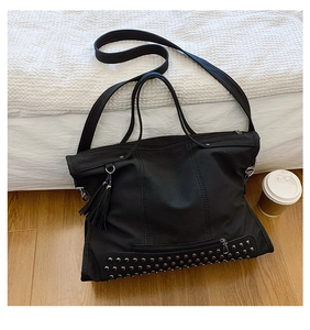 Close-up of black tote bag featuring silver studs, leather tassels and multi-pocket design