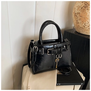 Detail of black tote bag with wrinkled texture, gold key pendant, and silver hardware