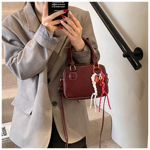 Detail of dark red Boston bag with white stitching and decorative charms on a grey blazer
