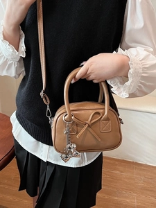 Borsa bowling retrò marrone con fiocco e ciondolo a cuore, portata come borsa a tracolla