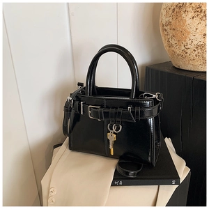 Detail of glossy black handbag featuring gold key charm and stylish belt buckle decor