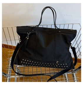 Close-up of black tote bag with silver studs and tassel detail in a metal basket