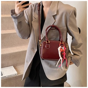 Detail view of burgundy leather crossbody bag with white stitching and woven charm