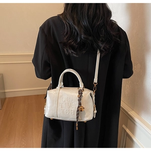 Detail of cream Boston bag with embossed CULTIVATOR lettering and golden bell charm