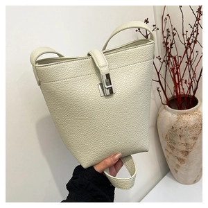 Close-up of litchi grain cream bucket bag with metal lock detail and leather strap