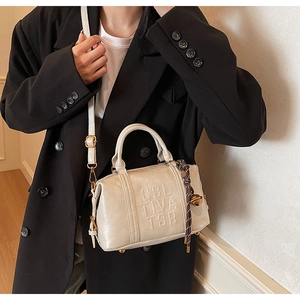 Detail of cream Boston bag with COL TIVA TOR embossing and woven bell charm accessory