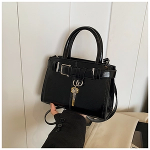 Detail of black glossy handbag with gold key charm and leather buckle strap details