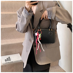 Detail of black rectangular crossbody bag with white stitching and colorful woven charm