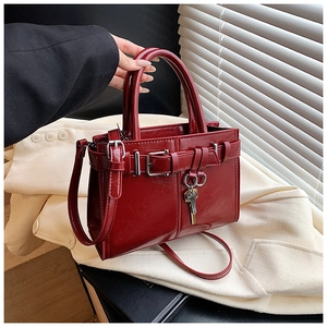 Detail of burgundy glossy leather handbag with golden key charm and metallic buckle closure