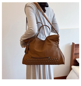 Brown tote bag detail with silver studs on base and decorative fringe tassel