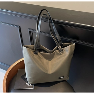 Détail d'un grand cabas en nylon vert olive avec anses noires posé sur un fauteuil