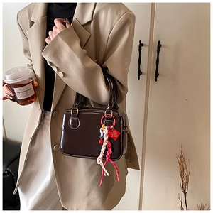 Chocolate glossy mini Boston bag with tassel charm shown on model in khaki suit