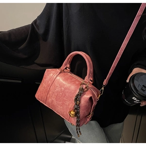 Pink vintage texture Boston bag with woven bell charm and long strap in lifestyle setting