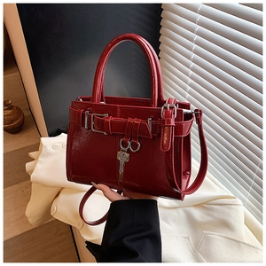 Detail of burgundy glossy leather handbag featuring silver key charm and sleek metal buckle