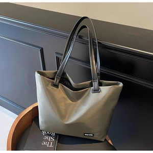 Sac de voyage vert olive avec poignées en cuir noir posé sur une chaise en bois