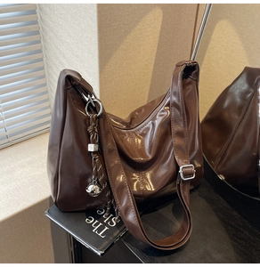 Detail of a large dark brown crossbody hobo bag with striped cord charm and silver hardware
