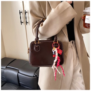 Detail of glossy brown leather Boston handbag with white stitching and gold hardware