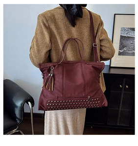 Detail of burgundy leather tote bag featuring metal rivets, tassel, and adjustable strap