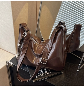 Detail of a dark brown hobo bag in glossy leather with silver buckles and a round charm