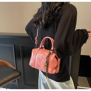Detailed view of coral pink Boston bag with textured leather and woven charm strap
