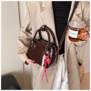 Detail of dark brown leather Boston bag featuring white stitching and woven charm