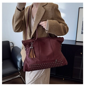 Detail view of burgundy leather tote bag featuring rivet studs and decorative tassels