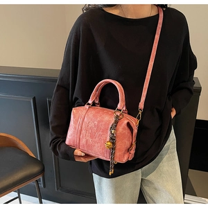 Close-up of pink textured leather bag with embossed letters and woven charm detail