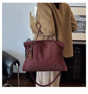 Detail of burgundy vintage tote bag with tassel accent and metallic studs on soft matte leather