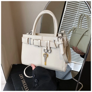 Detail of cream polished leather handbag featuring bronze key charm and dual handles
