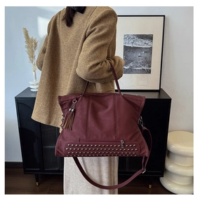 Detail of burgundy tote bag with metal rivets, leather texture, and tassel ornament