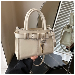 Detailed close-up of cream square handbag with gold key charm and buckle strap decor
