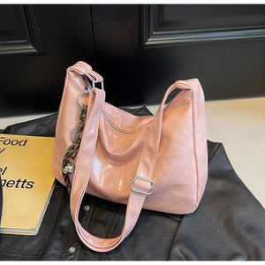 Detail of a pink glossy leather tote bag with side woven charm on a black jacket