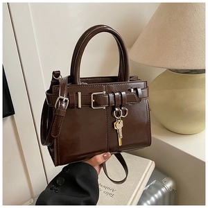 Detail of a deep chocolate faux leather handbag with silver buckle and golden key charm
