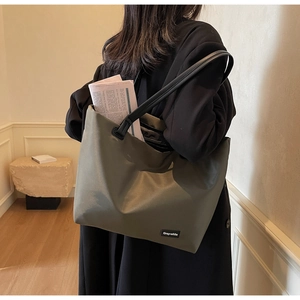 Détail d'un grand sac cabas vert olive avec lanières en cuir noir porté à l'épaule