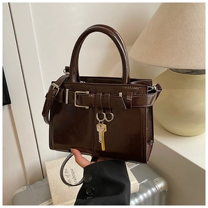 Close-up of a brown patent leather handbag featuring a metal key charm and buckle strap