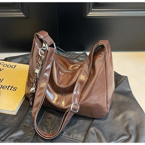 Macro shot of large brown glossy tote bag featuring silver hardware and decorative charm