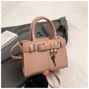 Detail of light pink square handbag with decorative metal buckle and key charm