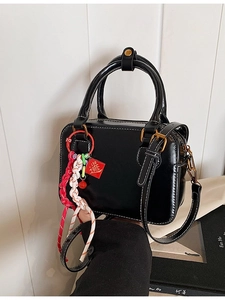 Chic black Boston bag with white stitching and detachable shoulder strap in city setting