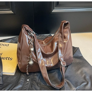 Macro detail of dark brown glossy leather tote featuring a silver buckle and bell charm
