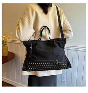 Detail view of large black tote bag with silver studs and side fringe tassel detail