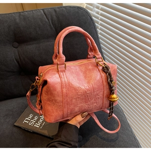 Close-up of pink cracked leather boston bag with Soliva embossed text and charm