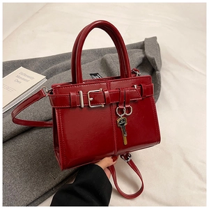 Close-up of red patent leather small square bag with gold key pendant and belt buckle detail