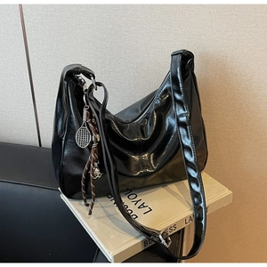 Detail of glossy black leather tote bag with silver tennis racket charm and zipper closure