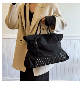 Detail of black vintage tote bag with metal studs and tassel on beige winter coat