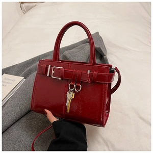 Detail of burgundy glossy patent leather tote bag with decorative key pendant and metal buckle