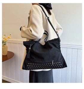Detailed view of black tote bag with silver studs and tassel on beige coat model