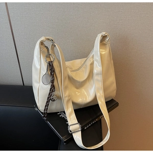 Detail of creamy white patent leather tote with adjustable strap and tennis racket charm