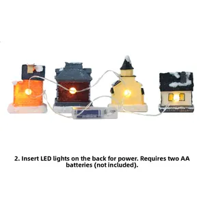 Detail of four miniature resin Christmas houses with snow-covered roofs and LED light string