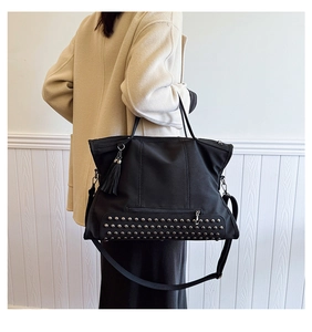 Detail of black large tote bag featuring silver rivet base and stylish side tassels