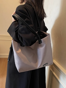 Grand sac de voyage gris-blanc avec anses en cuir noir porté par un mannequin en scène